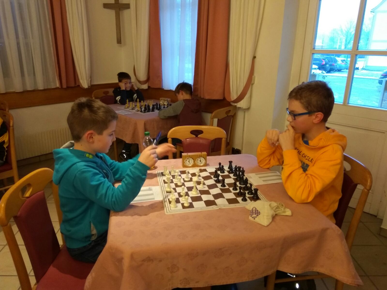 Zwei Kinder in einer Partie mit Schachuhr, im Hintergrund spielen zwei weitere an einem zweiten Brett